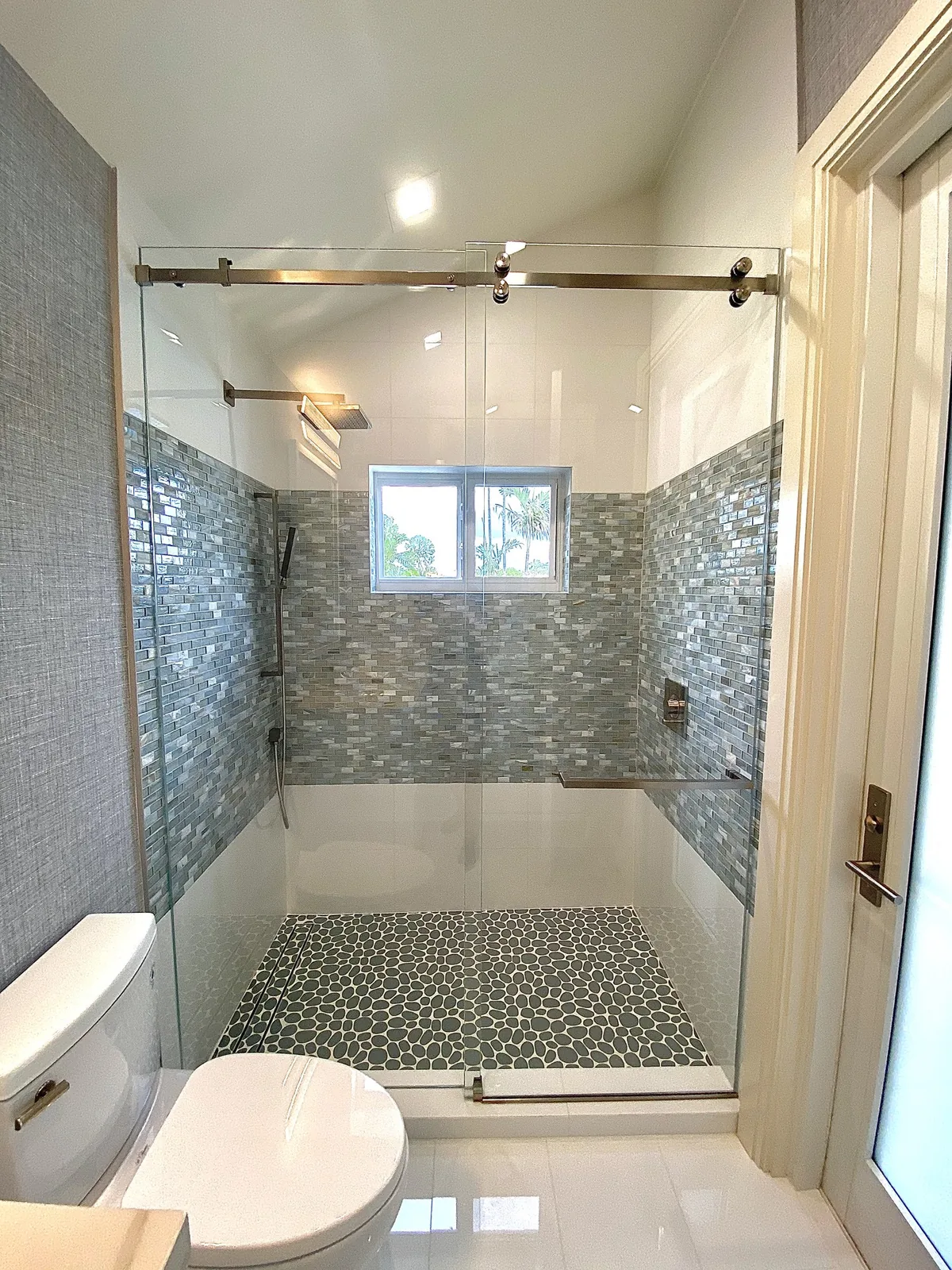 Walk-in shower with glass enclosure, gray tile surround, and river-stone floor detail.