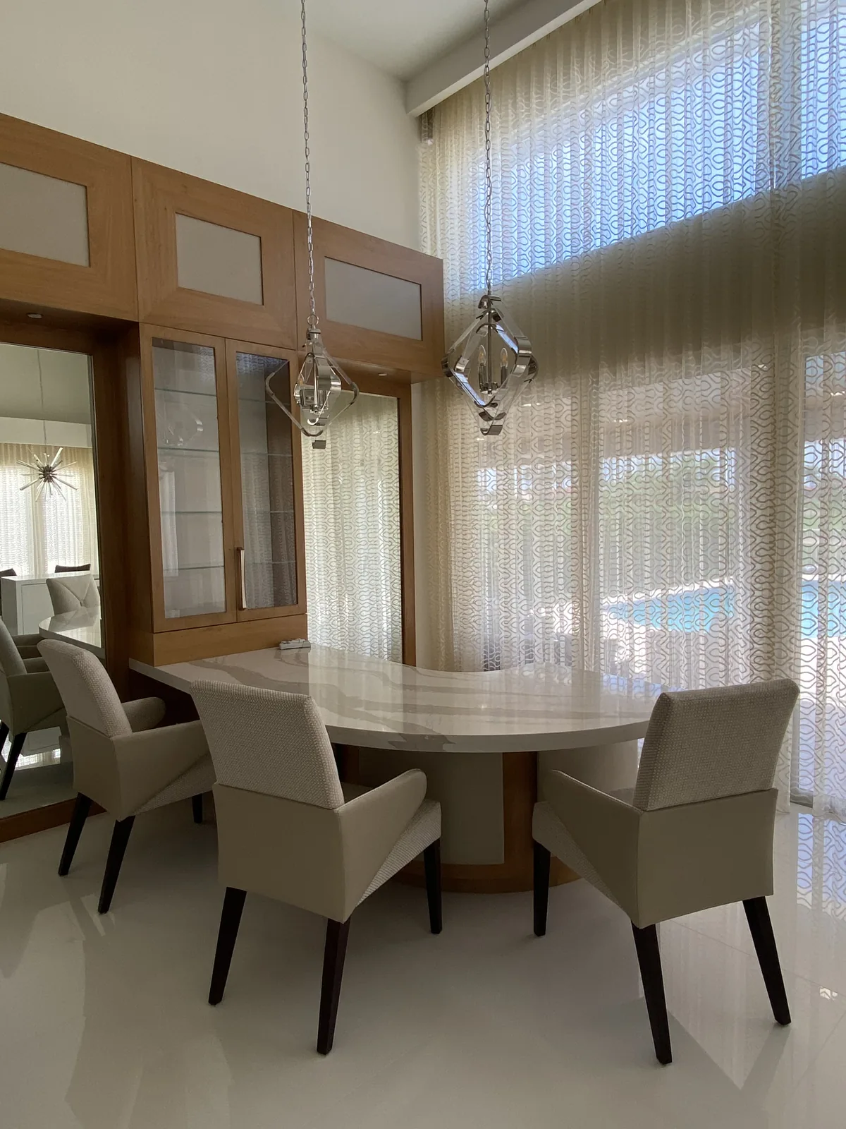 Curved white table, beige upholstered chairs, pendants, and patterned curtains.