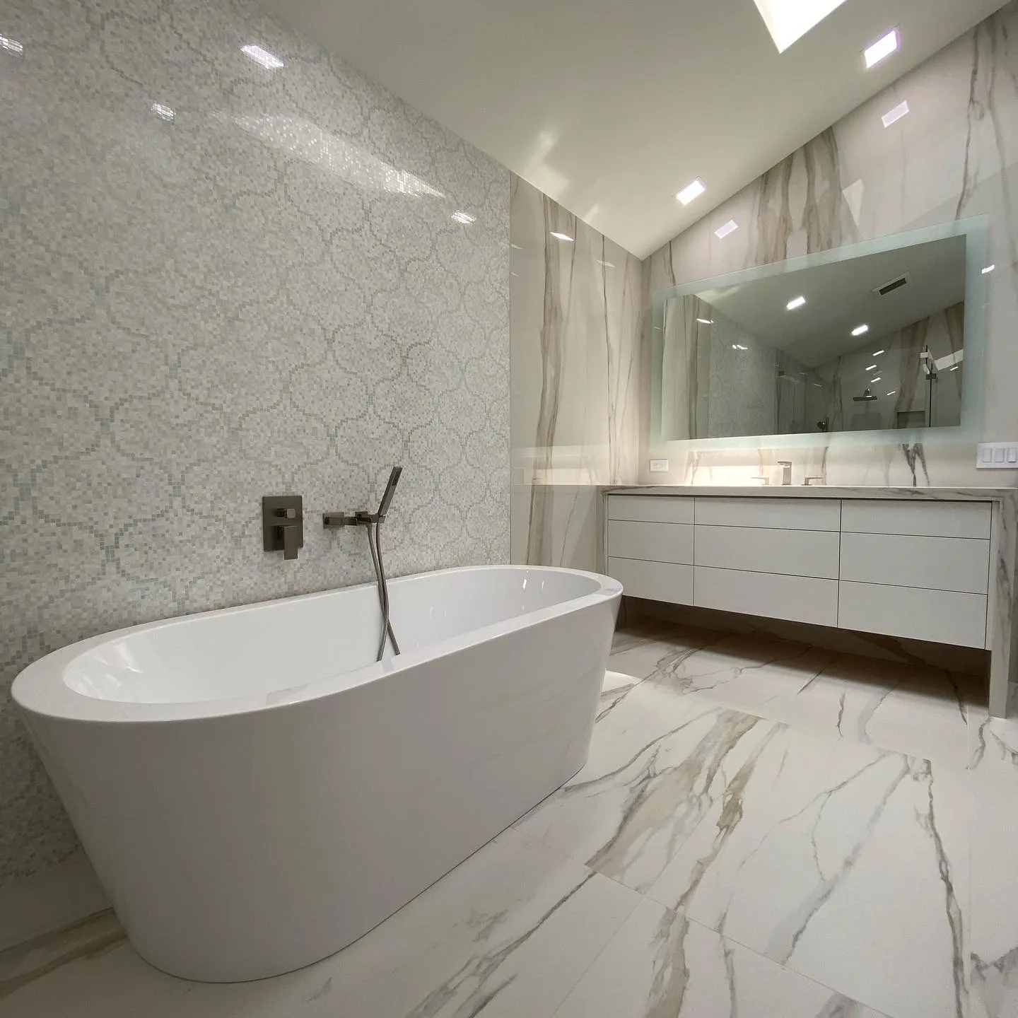 Freestanding white tub, marble flooring, mosaic accent wall, custom vanity.