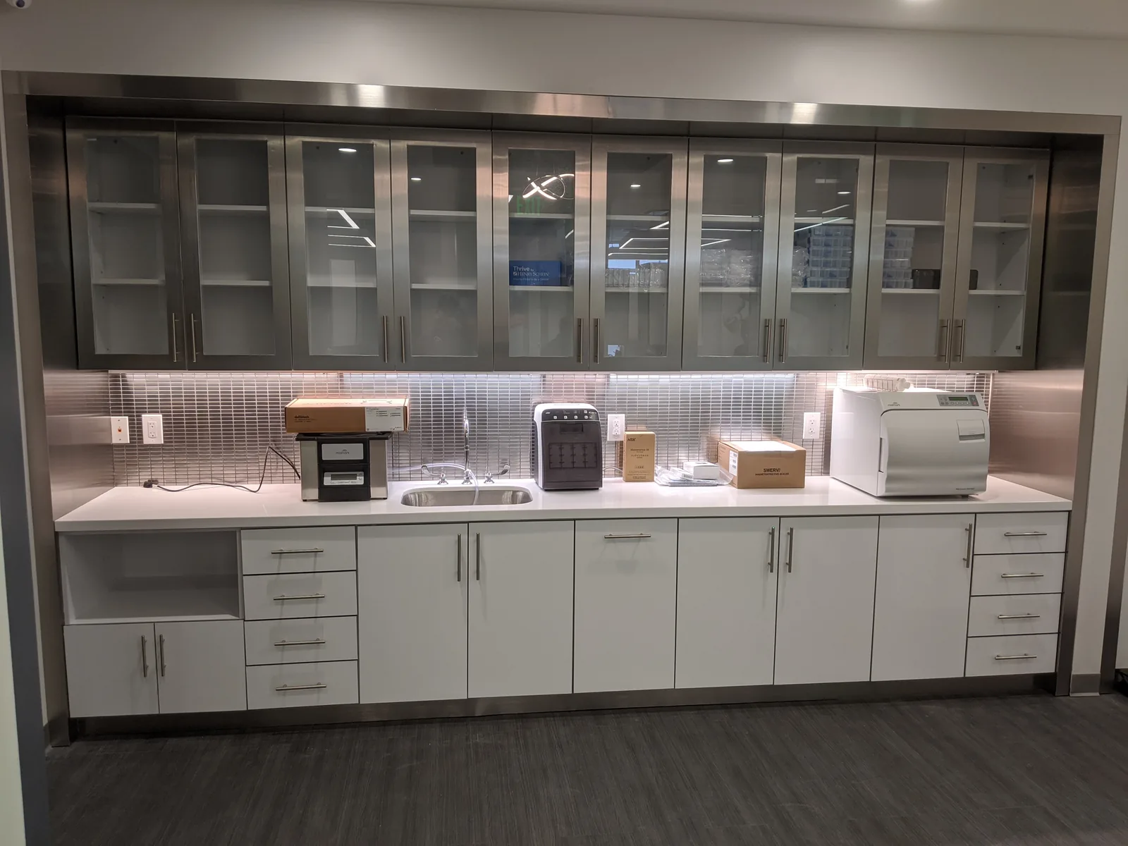 Office kitchen with white cabinetry, stainless countertop, and built-in appliances.