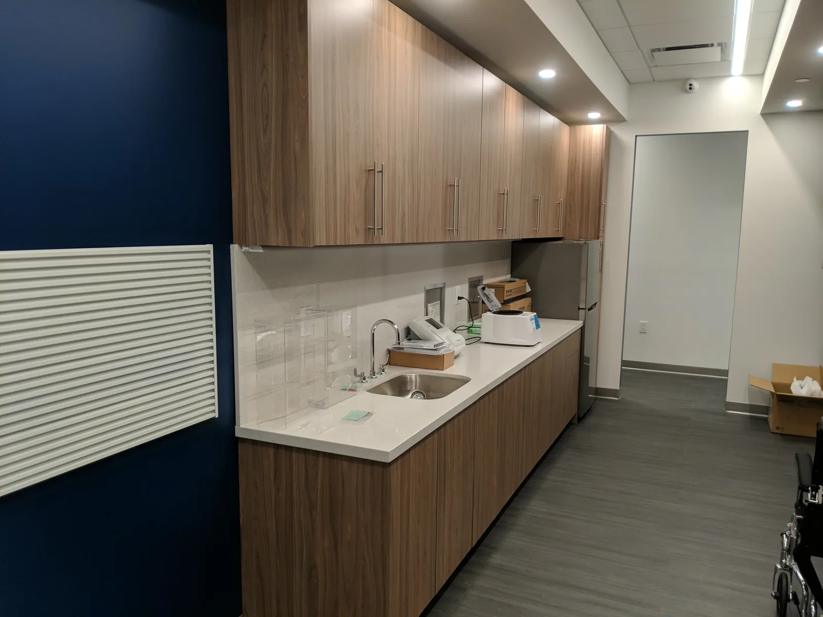 Office kitchen with wood cabinetry, white countertops, and tile backsplash.