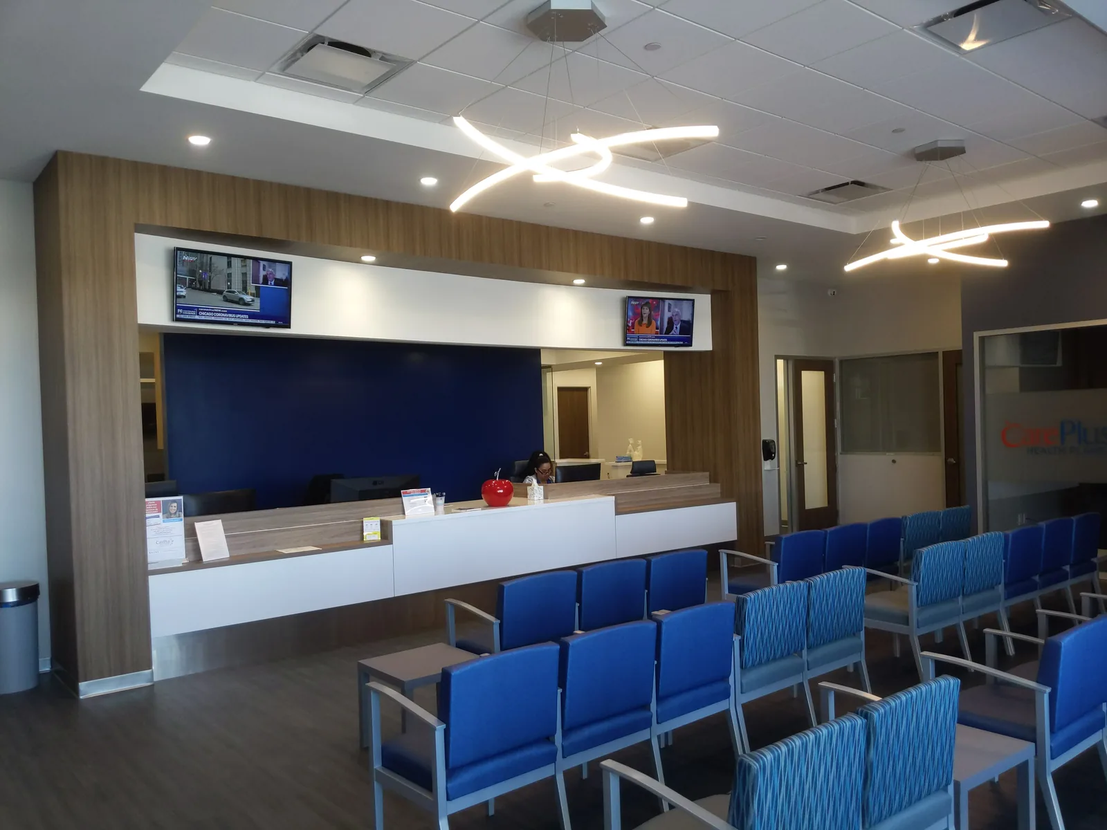 Medical clinic reception with blue seating, wood paneling, contemporary pendants.