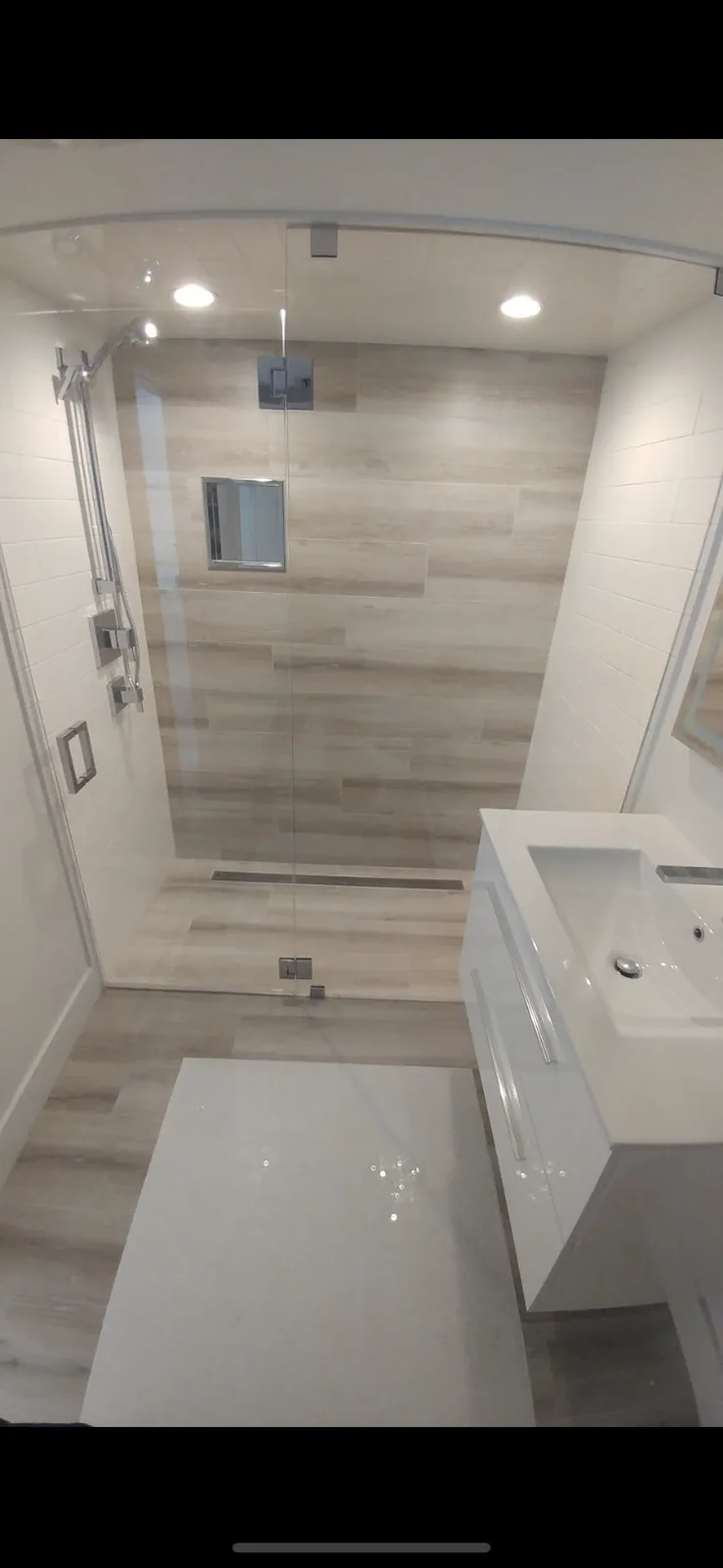 Walk-in shower with wood-look tile and frameless glass enclosure.