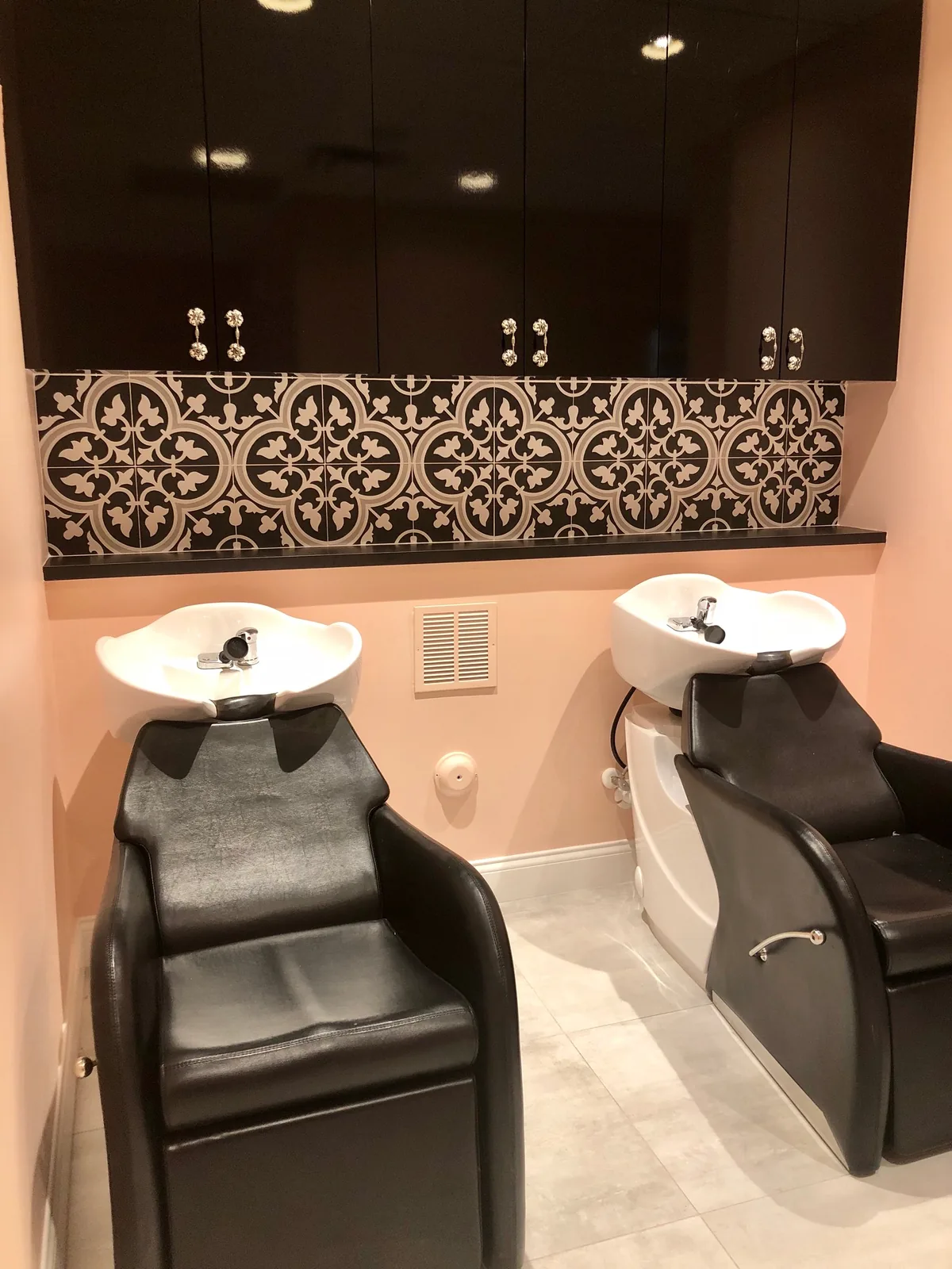 Salon shampoo station with black chairs and black-and-white tiled backsplash.