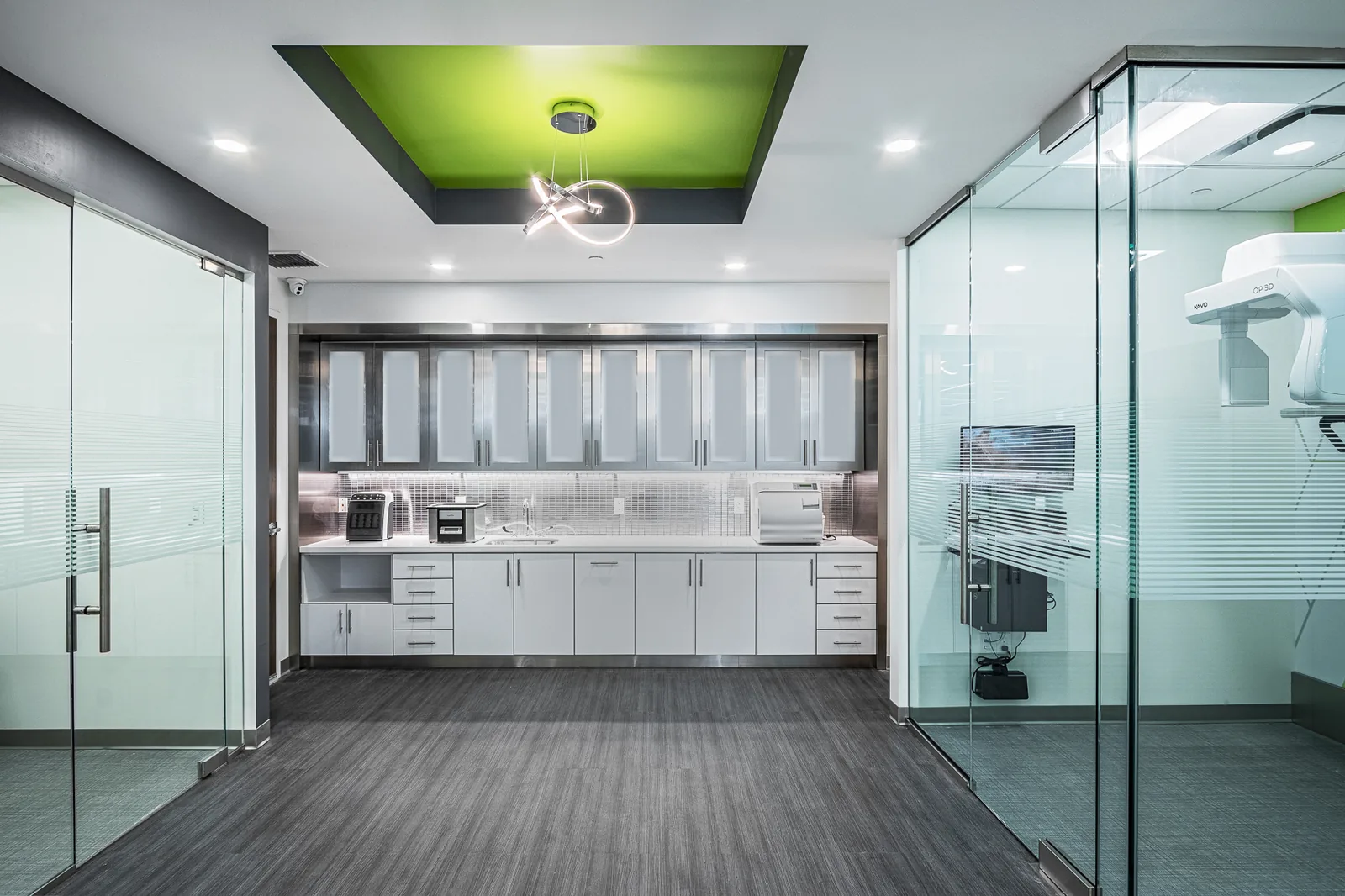 Dental interior with white cabinetry, glass partitions, and green ceiling accent.