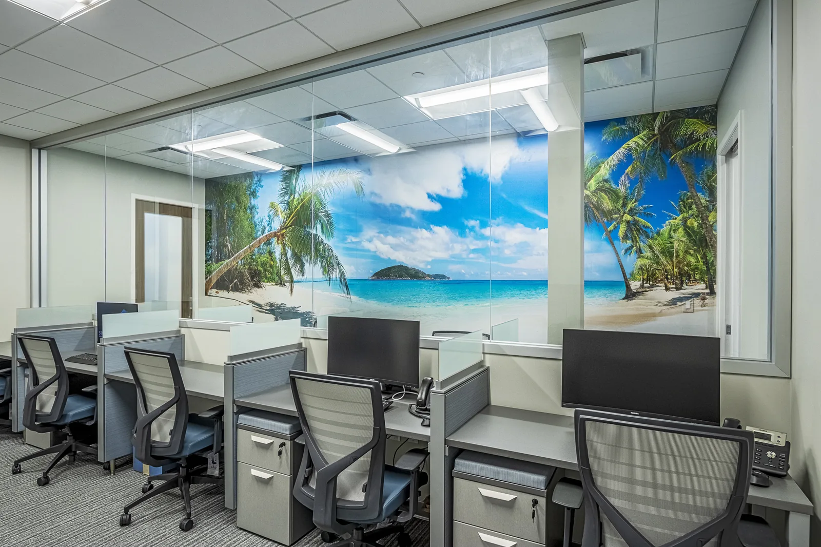 Office workstations with tropical beach mural wall in commercial tenant buildout.