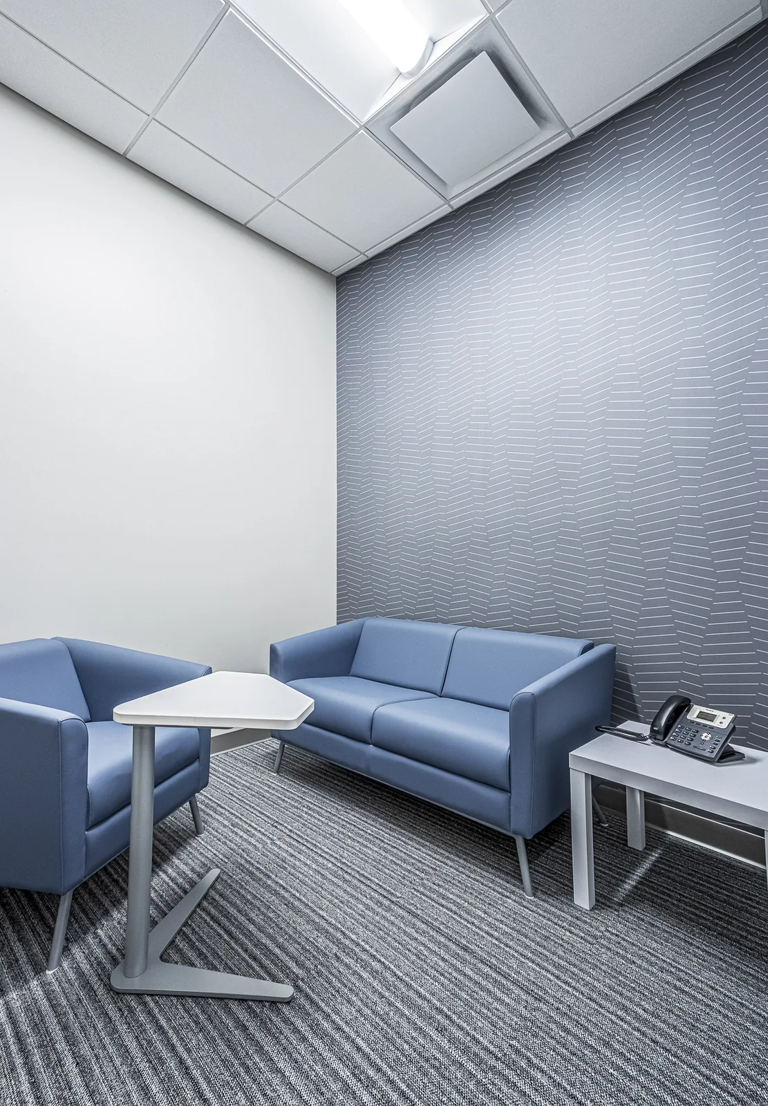 Meeting room with blue seating, white table, gray textured wall.